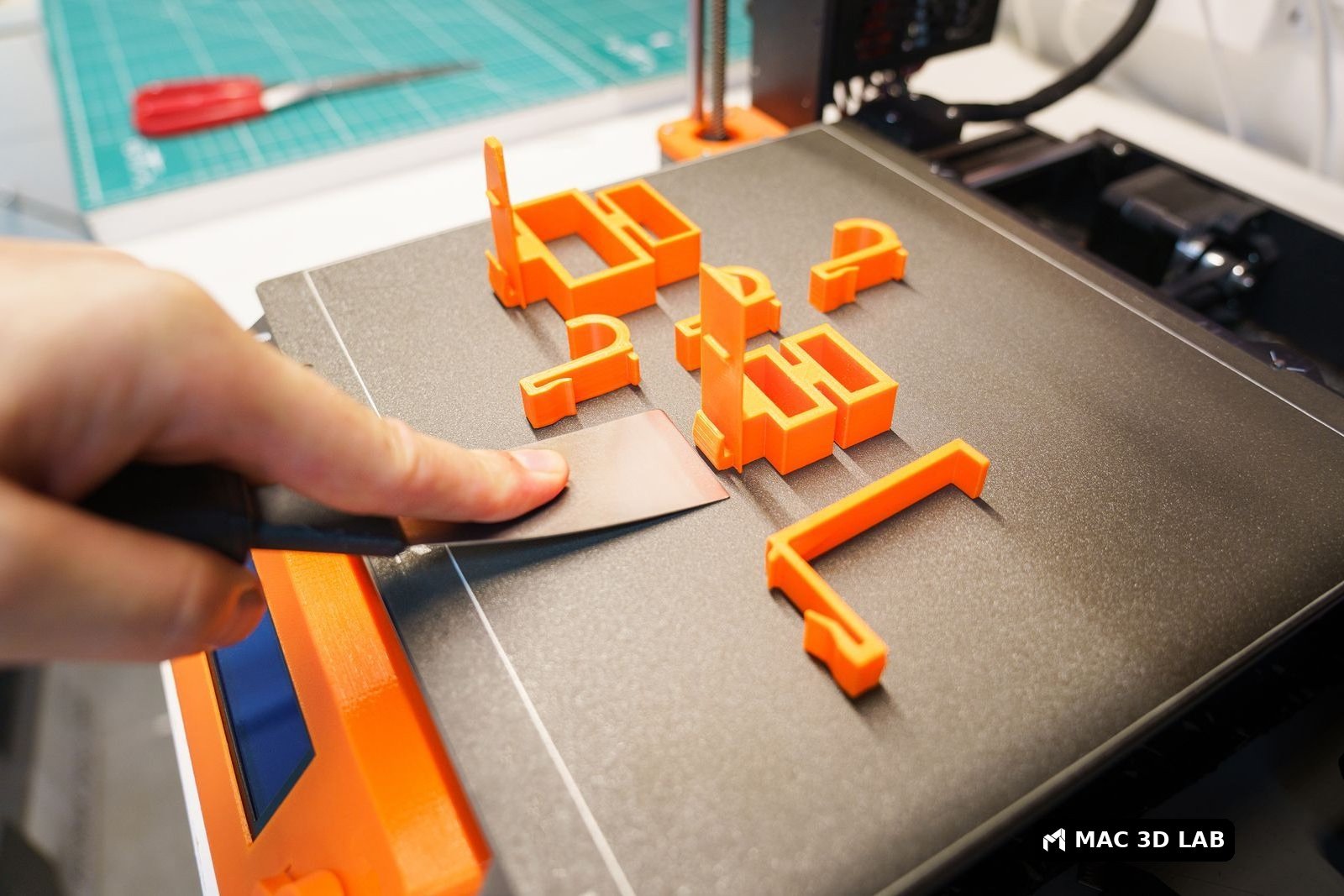 Retirando una pieza naranja impresa en 3D de la cama